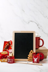 Christmas gift mockup web banner. Xmas holiday gift for everyone. Empty black board and Red and brown zero waste cup, shopper bag, socks, notepad, sweets, cookies on table