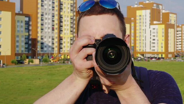 Positive young tourist man or student photographer takes pictures with a mirrorless camera to create memories. Man travelling in strange city, smiling, shooting urban landmarks. Front view