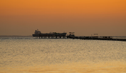 Obraz premium cargo vessel ship crossing the sea during sunrise, view from a beach resort. Transportation by the sea industry.