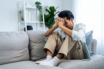 Asian young upset depressed man sitting alone in living room at home. 