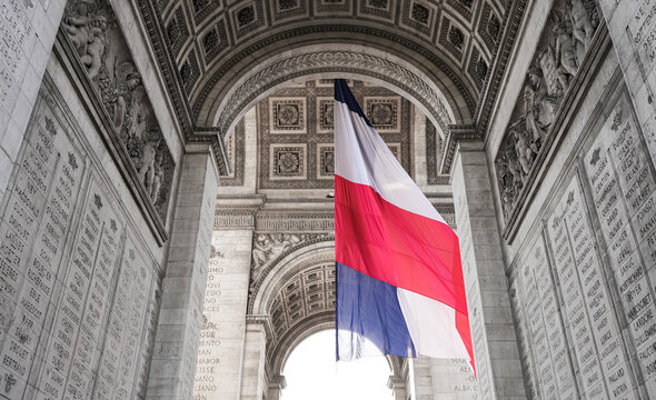 Wide angle photo with the National Flag of France waving under the Arch of Triumph landmark building during Armistice Day.