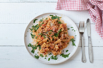 Pasta with tomato sauce, tuna and parmesan cheese on  a plate on white wooden background