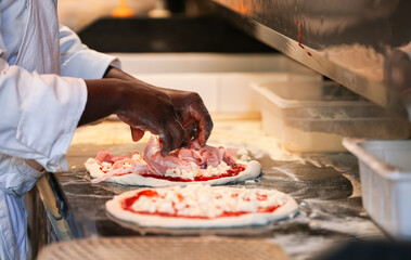 A chef prepares a prosciutto and champignons pizza inside an Italian restaurant. Photo with the moment when he adds the ingredients.A chef prepares a prosciutto and champignons pizza inside an Italian