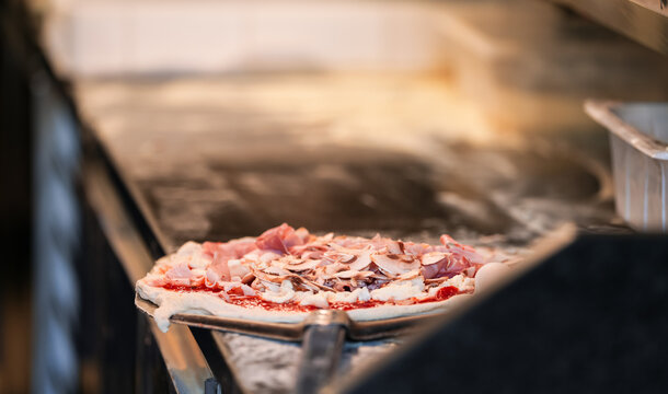A chef prepares a prosciutto and champignons pizza inside an Italian restaurant. Photo with the moment when he adds the ingredients.