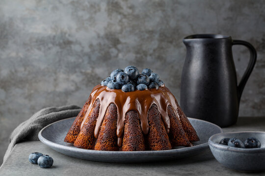 Chocolate marble cake baked in a Pudding baking mold, with chocolate glaze, blueberries. Dark grey background.