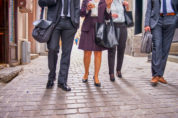 Business meeting outdoor, four people walking along city streets. Detail on the legs
