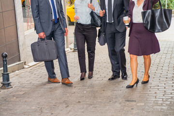 Business meeting outdoor, four people walking along city streets. Detail on the legs