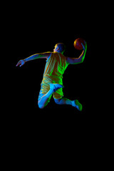 Active athletic male basketball player jumping with basketball ball isolated over dark background in blue neon light. Concept of energy, professional sport, hobby.