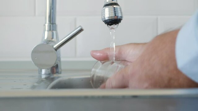 Man Washing and Cleaning Dishes in the Kitchen Sink with Clean Water.  Shooting with a Person Cleaning a Glass 
