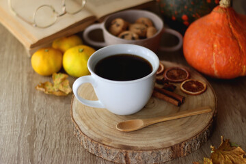 Obraz na płótnie Canvas Cup of tea or coffee, seasonal spices, bowl of cookies, blanket, pumpkins, colorful leaves, books and tangerines on wooden table. Cozy hygge at home. Selective focus.