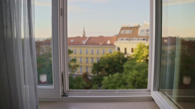 Slow push on open window in hotel or apartment building during sunset or sunrise. Quiet neighborhood in afternoon sunlight. Window open for fresh air or break in robbery. Mysterious and dramatic move 