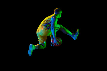 Fototapeta na wymiar Active athletic male basketball player jumping with basketball ball isolated over dark background in blue neon light. Concept of energy, professional sport, hobby.