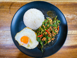 Rice topped with stir-fried pork and basil with a fried egg on the table