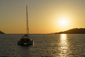 Sunset with a yacht on the tropical mediterranean sea. Evening or morning landscape with beautiful orange sun, calm water and soft light in summer