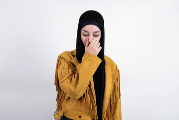 young beautiful muslim woman wearing hijab and yellow jacket over white background, holding his...