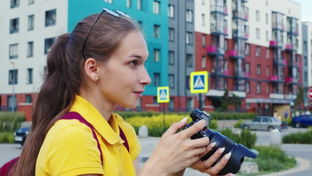 Positive student girl takes pictures of sightseeing attractions while travelling in strange city. Young woman smiling, shooting urban landmarks. Photographer takes pictures to create memories