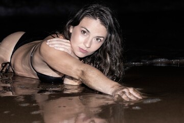 Fototapeta premium Fashion shot of a beautiful girl in a black bikini lying on the beach