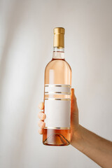 Male hand holds big bottle of pink wine or rosa champagne with no brand label, mockup template. Vertical shot, white background