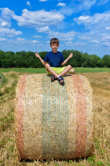 Naklejka na ściany i meble The boy is sitting on golden hay bales on the field