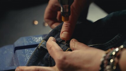 A tailor seamstress inserts metal rivets on jeans with a special machine in workshop repairing old denim clothes. Small family business, tailoring and repair of clothes, handmade. Close-up