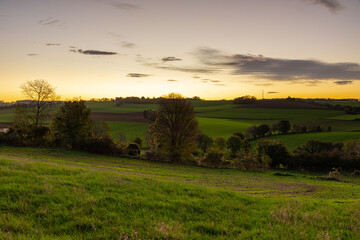 Obraz premium Spectacular and colourful sunrise over a rolling hill landscape with winding roads and agricultural fields in the south of Limburg. The landscape reminds of the Tuscan region in Italy.