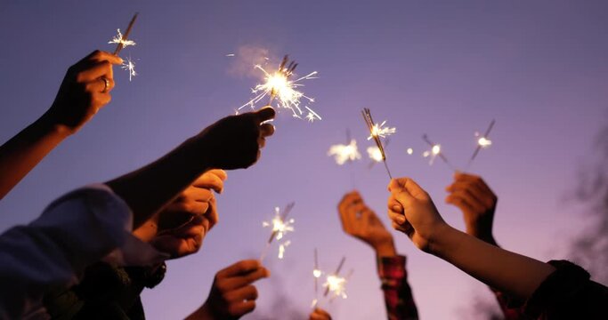 Selective focus, Close up group of hands holding fire burning sparklers and raising on sky in New year party