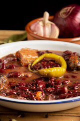 Close-up detail of Basque beans on a rustic table with onions, garlic and green chilli, selective focus, vertical