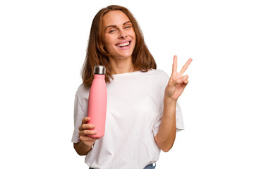 Young caucasian woman holding a pink thermo isolated joyful and carefree showing a peace symbol with fingers.