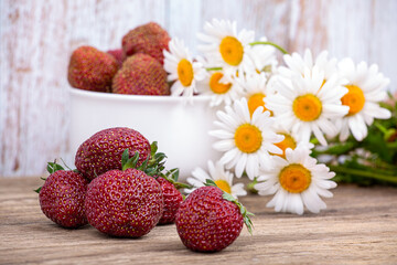 Large ripe strawberries on the background of a plate with berries and a bouquet of daisies. Macro photography
