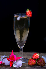 A misted glass of champagne, fresh strawberries and pieces of ice on a dark background