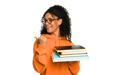 Young student woman holding a pile of books isolated points with thumb finger away, laughing and...