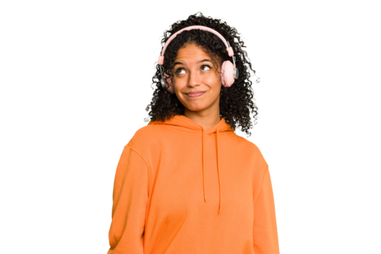 Young Brazilian woman listening to music with headphones isolated dreaming of achieving goals and purposes