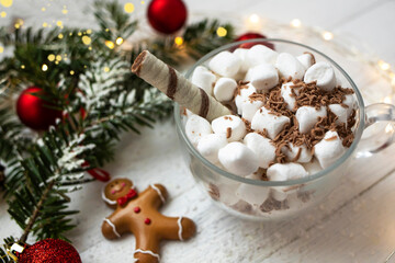Christmas background. Cup of hot chocolate with marshmallows on a white wooden background with a gerland and a spruce branch.