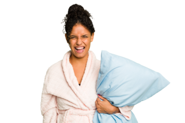 Young brazilian woman wearing a pajama holding a pillow isolated screaming very angry and aggressive.