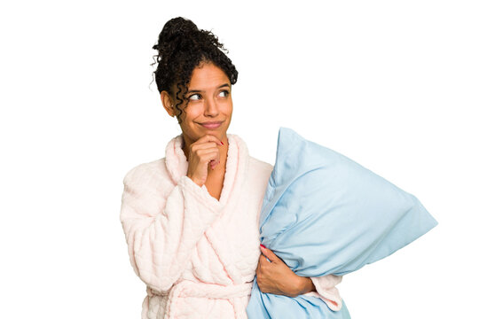 Young brazilian woman wearing a pajama holding a pillow isolated looking sideways with doubtful and skeptical expression.