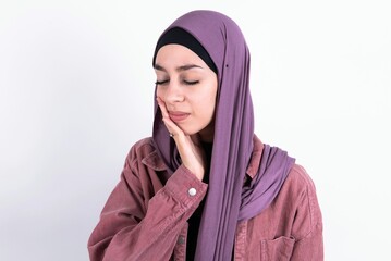 young beautiful muslim woman wearing hijab against white background with toothache