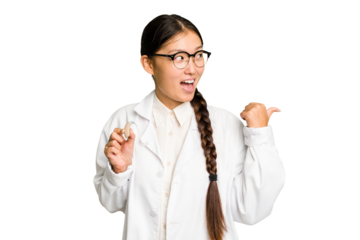 Young asian otorhinolaryngologist woman holding a hearing aid isolated points with thumb finger away, laughing and carefree.