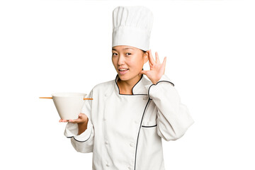 Young chef asian woman holding a bowl of ramen isolated trying to listening a gossip.