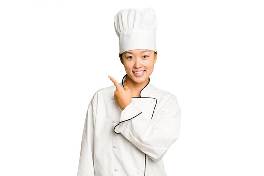 Young asian cook woman isolated smiling and pointing aside, showing something at blank space.