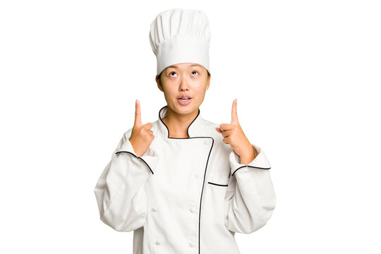 Young asian cook woman isolated pointing upside with opened mouth.