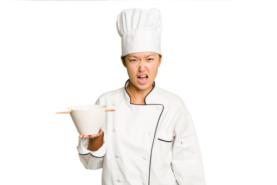 Young chef asian woman holding a bowl of ramen isolated screaming very angry and aggressive.