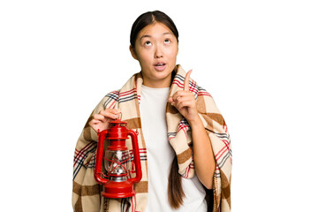 Young asian woman wearing a blanket and holding a lamp isolated pointing upside with opened mouth.