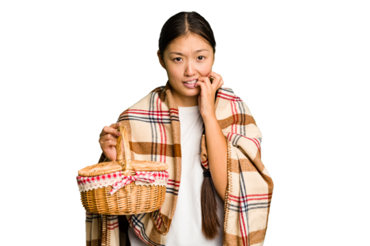 Young asian woman holding a picnic basket isolated biting fingernails, nervous and very anxious.