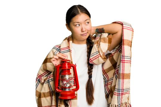 Young asian woman wearing a blanket and holding a lamp isolated touching back of head, thinking and making a choice.