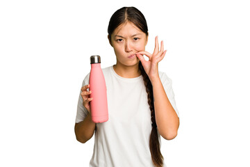 Fototapeta premium Young asian woman holding a pink thermo isolated with fingers on lips keeping a secret.