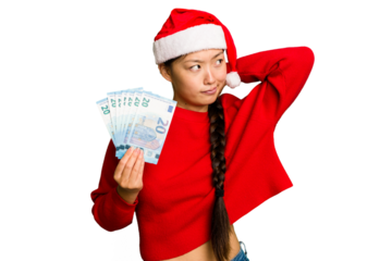 Young asian woman celebrating Christmas holding banknotes isolated touching back of head, thinking and making a choice.