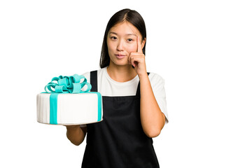 Young asian bakery holding a birthday cake isolated pointing temple with finger, thinking, focused on a task.