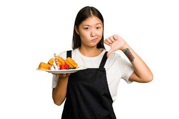 Young asian waitress woman holding waffles isolated showing a dislike gesture, thumbs down. Disagreement concept.