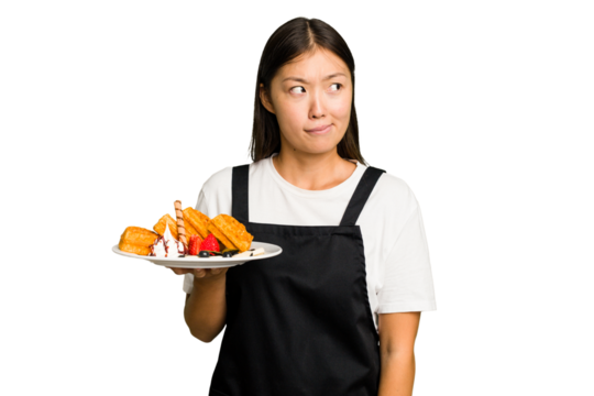 Young asian waitress woman holding waffles isolated confused, feels doubtful and unsure.