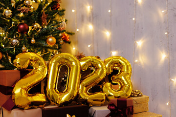 Happy new year concept - close up of golden 2023 foil air balloon numbers near Christmas tree